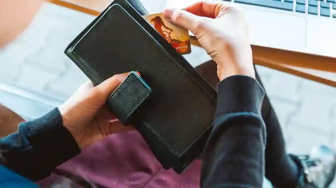 Person holding a black wallet and pulling out a Mastercard credit card, while seated. 