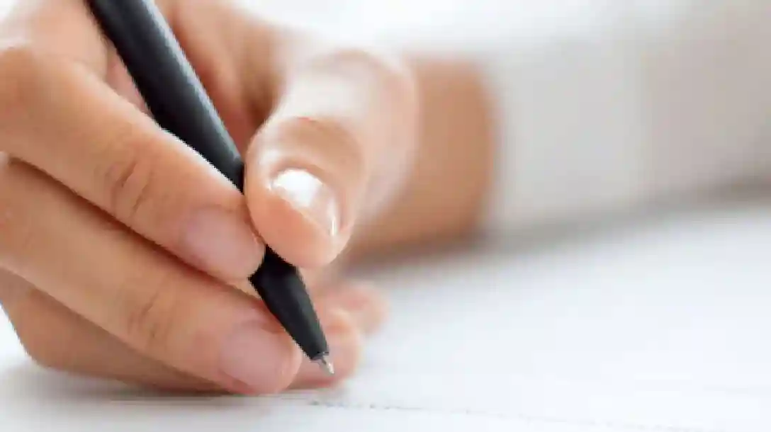 Person writing on paper, with a black pen, wearing a white shirt.