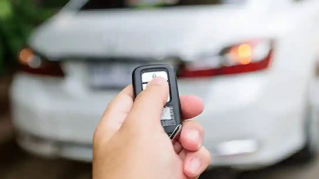 Person holding a key fob, pointing it towards a white car. 