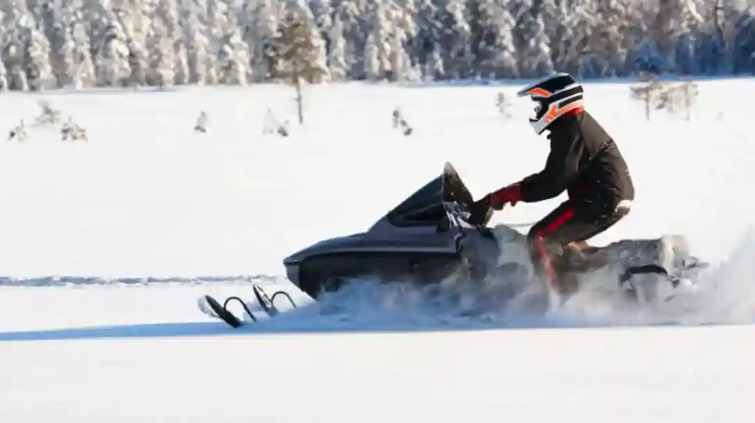 Snowmobile being driven through the snow by a driver wearing a helmet with orange strips.