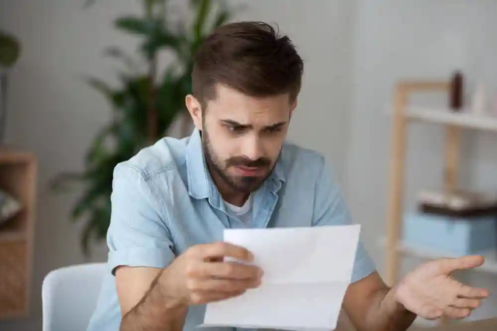 confused looking person in blue shirt looking at a piece of paper, sitting in a white chair