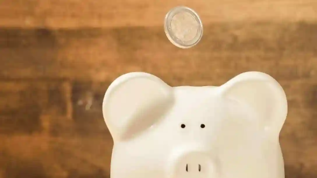 Piggy bank with a coin falling and a wooden background.